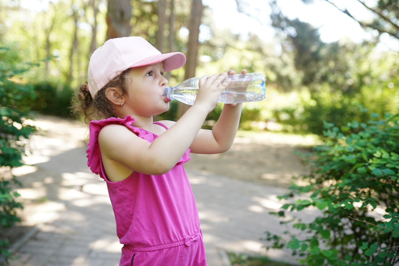 enfant canicule Une jeune fille porte une casquette et bois de l'eau