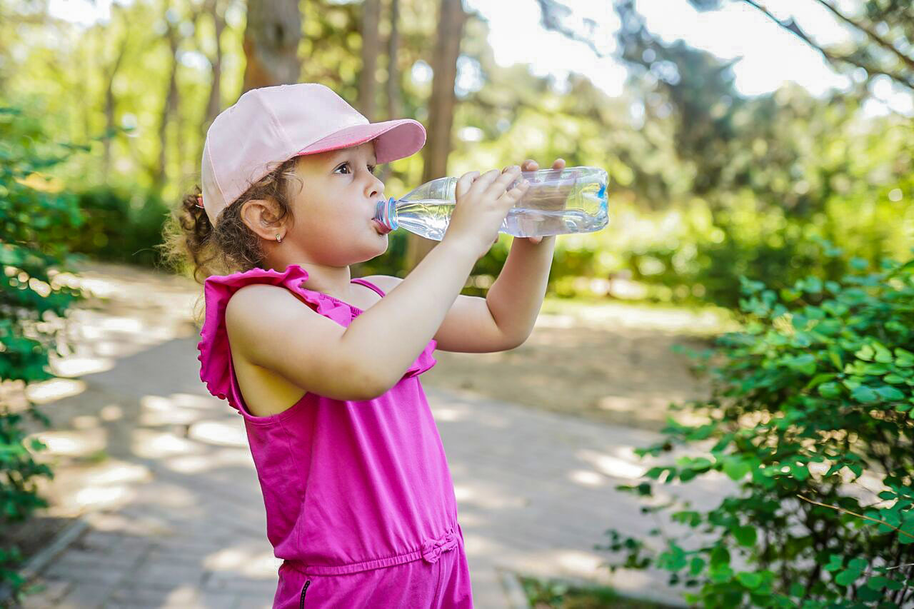 enfant canicule Une jeune fille porte une casquette et bois de l'eau